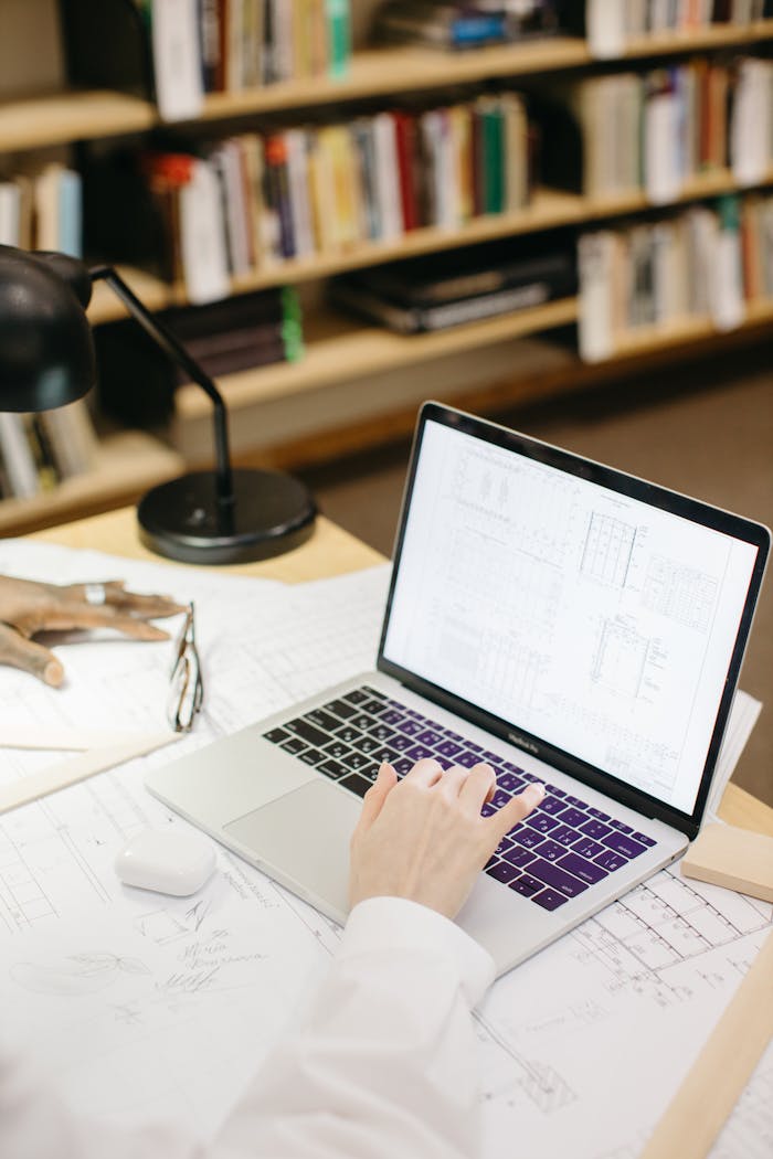services-04 Architect working on laptop with design plans in a modern workspace.